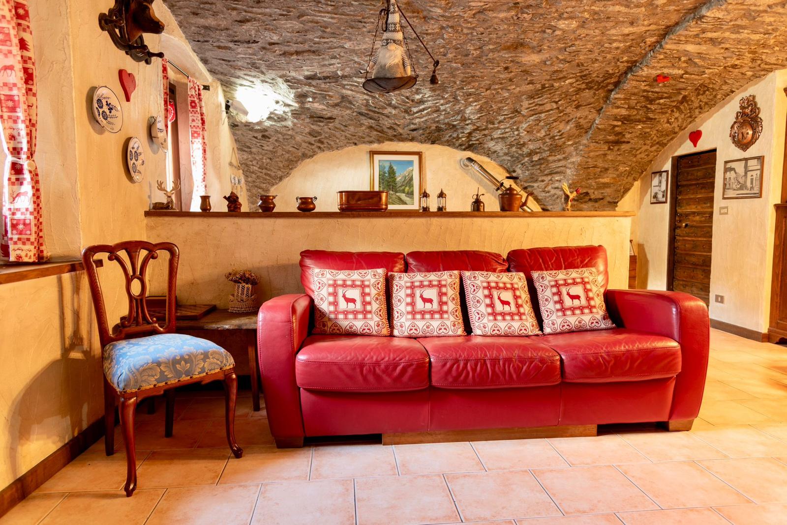 Soggiorno con volta in pietra a vista, divano rosso e decori tradizionali