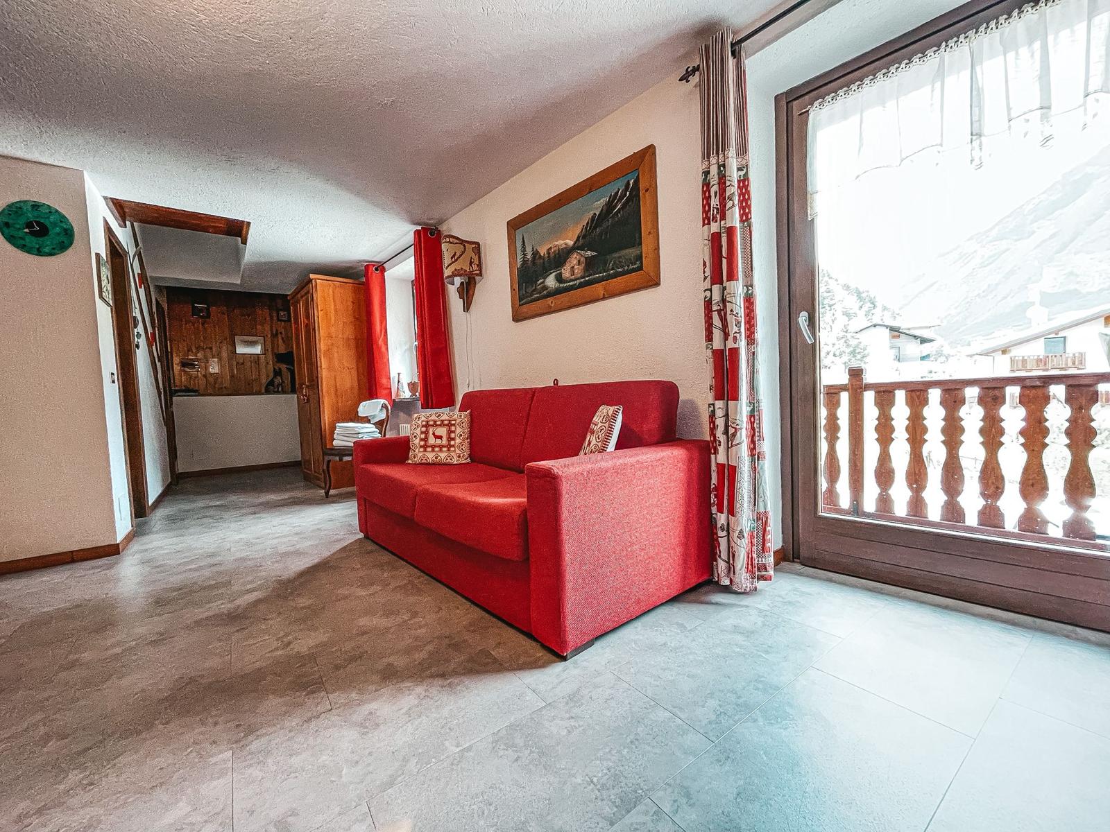 Salotto con divano rosso e portafinestra sul balcone con vista montagna