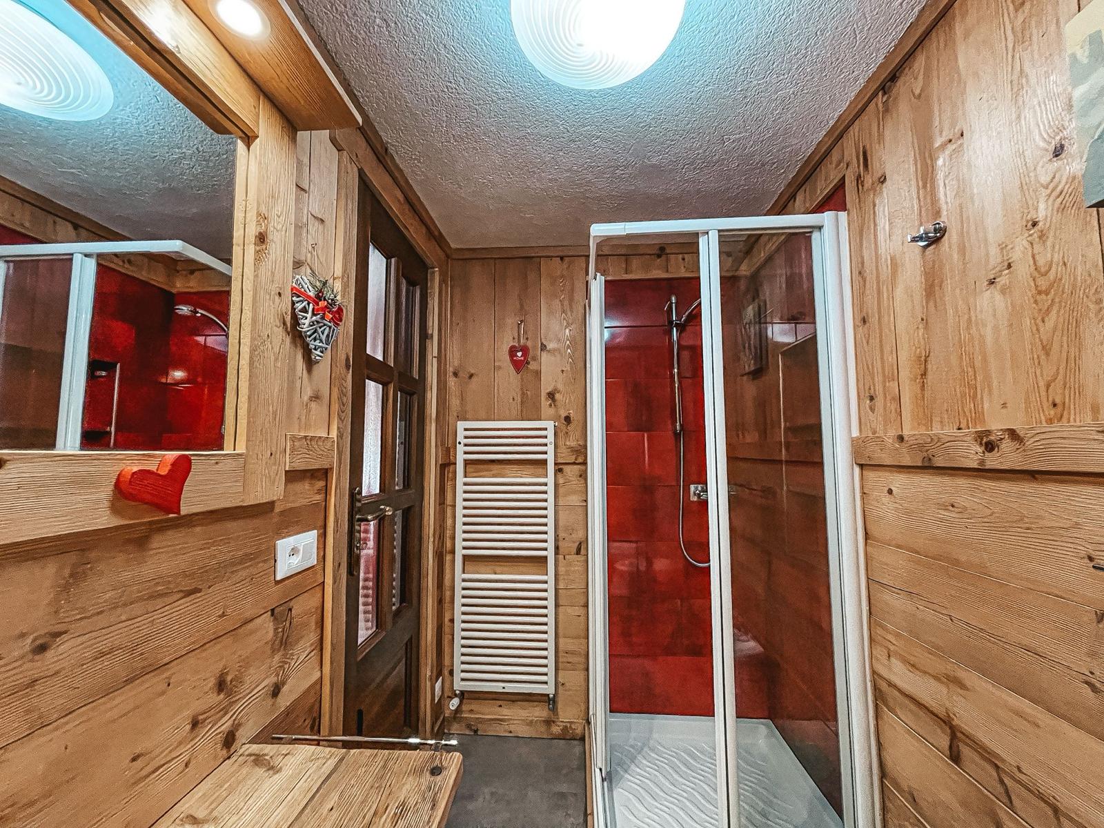 Bagno con doccia rivestita in piastrelle rosse e boiserie in legno
