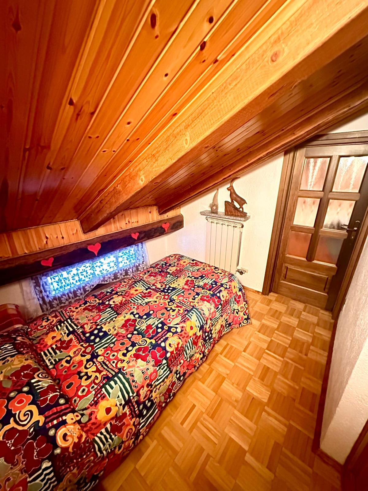 Camera in mansarda con perlinato in legno e copriletto a fiori