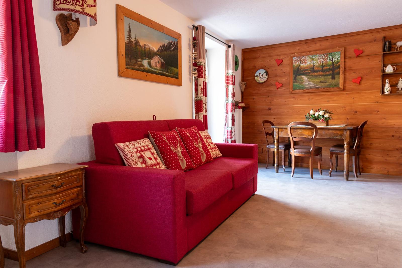 Soggiorno luminoso con divano rosso, boiserie in legno e tavolo da pranzo